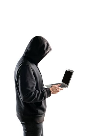 Isolated portrait of unrecognizable young man in black hoodie holding laptop. Concept of hacking and identity theftの写真素材