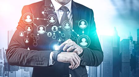Unrecognizable young manager using smartwatch in city with double exposure of HR icons. Concept of hi tech and social network. Toned imageの写真素材