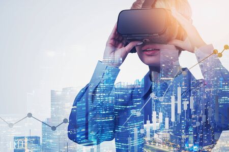 Young woman in VR glasses using it in night city with double exposure of digital charts. Concept of...