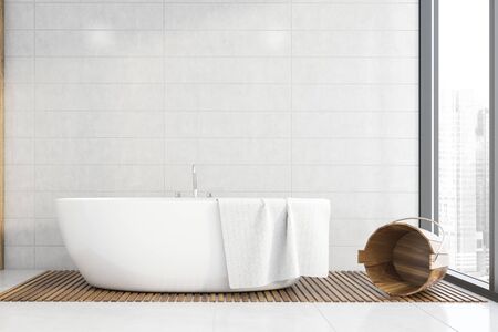 Interior of stylish bathroom with white tile walls and floor, comfortable white bathtub and wooden...