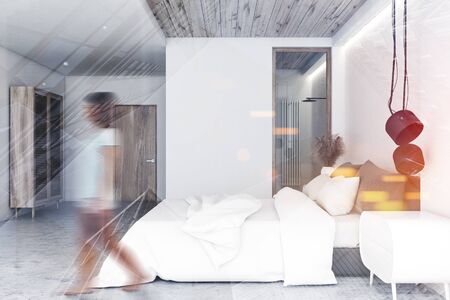 Blurry young woman walking in luxury bedroom interior with white walls, concrete floor, king size...