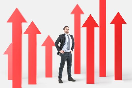 Confident bearded businessman standing among red arrows pointing up. Concept of growth and success.の写真素材