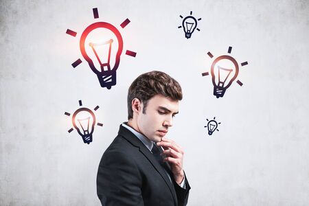 Side view of handsome young businessman standing near concrete wall with colorful light bulbs drawn...