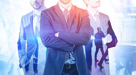Three confident young executives standing together in modern city with colleagues in background. Concept of leadership and corporate lifestyle. Toned image double exposureの写真素材