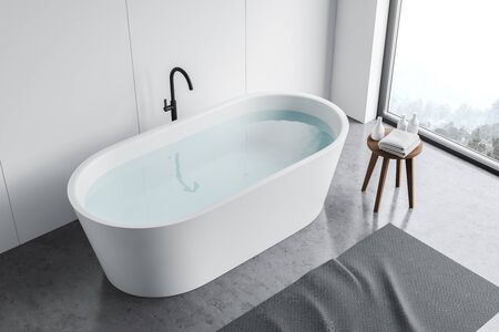 Top view of comfortable bathtub with water standing in modern bathroom with white panel walls,...