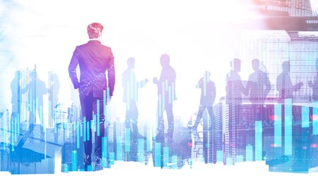 Rear view of young businessman walking in modern city with silhouettes of his colleagues in background with double exposure of digital graph. Concept of trading and leadership. Toned imageの写真素材