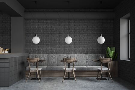 Interior of modern restaurant in loft style with gray brick walls, concrete floor, comfortable gray sofa and row of square tables with chairs near them. 3d renderingの写真素材
