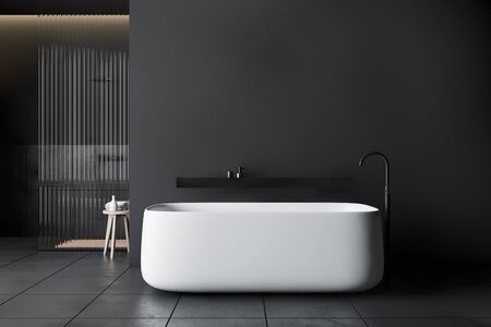 Interior of stylish bathroom with dark gray and tiled walls, tiled floor, comfortable bathtub with black shelf above it and shower stall with glass walls. 3d renderingの写真素材