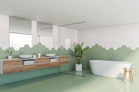 Corner of stylish bathroom with green hexagonal tile and white walls, comfortable white bathtub and...