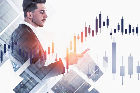 Side view of young businessman looking at smartphone in night city with double exposure of forex graph. Concept of business lifestyle and fintech. Toned imageの写真素材