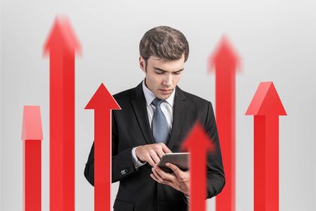Young businessman using tablet computer standing among blurry red arrows pointing up. Concept of growth and success.の写真素材