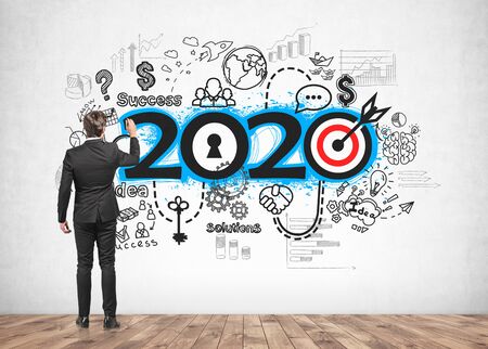 Rear view of young businessman drawing 2020 business strategy sketch on concrete wall. Concept of new year and planningの写真素材