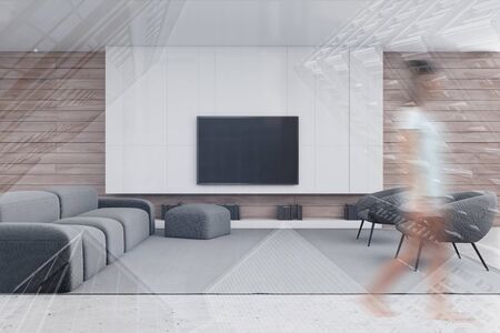 Blurry young woman walking in modern living room with white and wooden walls, concrete floor, comfortable gray sofa and armchairs and TV. Toned image double exposureの写真素材