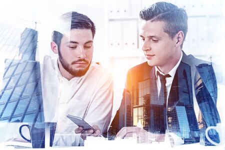 Two engaged young businessmen working in blurry city with double exposure of Moscow city panorama. Concept of teamwork and business lifestyle. Toned imageの写真素材