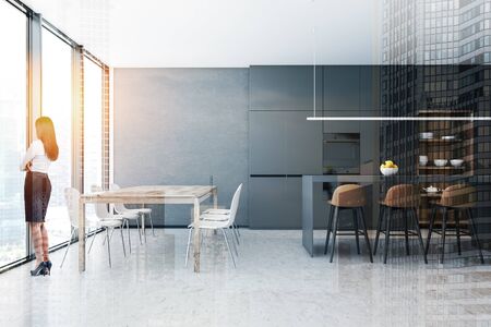Young woman standing in stylish kitchen with concrete walls and floor, bar with stools and wooden dining table with white chairs. Toned image double exposureの写真素材