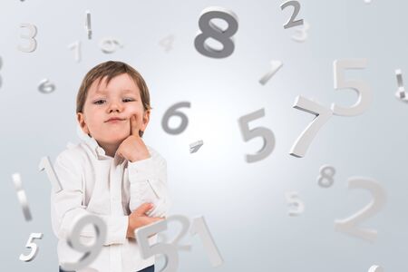 Smart little preschool boy in white shirt standing over white background with falling numbers....