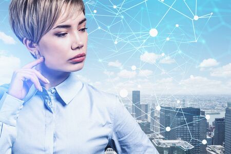 Pensive young Asian businesswoman standing over cityscape background with double exposure of blurry...