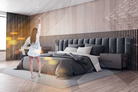 Woman in nightgown standing in master bedroom with wooden walls and floor, comfortable king size bed and beige bedside tables. Toned image double exposureの写真素材