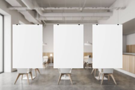 Three blank mock up posters hanging in blurry modern industrial style pub with white and wooden walls, concrete floor and rows of square tables with white and gray chairs 3d renderingの写真素材