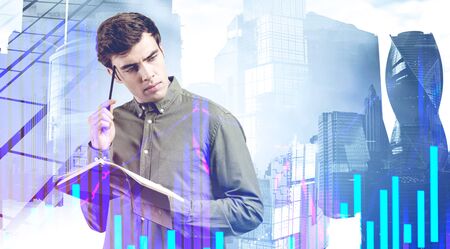 Pensive young businessman with notebook standing in abstract city with double exposure of digital...