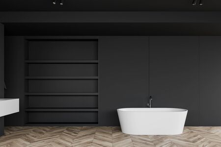 Interior of spacious bathroom with dark gray walls, wooden floor, comfortable bathtub with black shelves near it and ceiling lamps. 3d renderingの写真素材