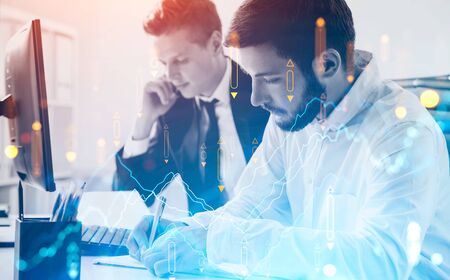 Two European businessmen working together in blurry office with double exposure of digital chart....