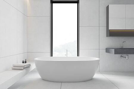 Interior of modern bathroom with white tiled walls and floor, comfortable bathtub standing near the...