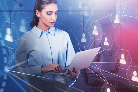 Serious young businesswoman working with laptop in blurry office with double exposure of social...