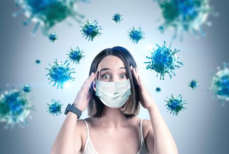 Scared young woman in protective mask standing near grey wall with blurry blue viruses around her....