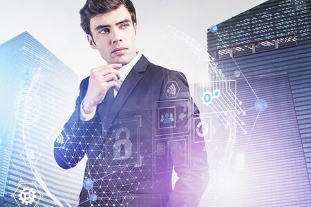 Pensive European businessman standing in abstract city with double exposure of creative immersive futuristic digital interface. Concept of hi tech and internet connection. Toned blurry imageの写真素材