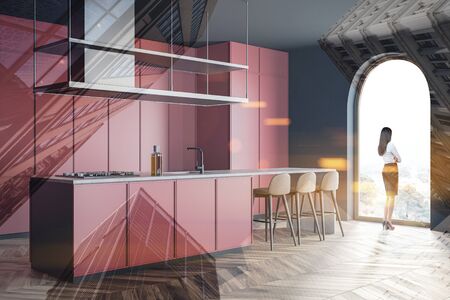 Young woman standing in stylish spacious kitchen with red and grey walls, wooden floor, red island...