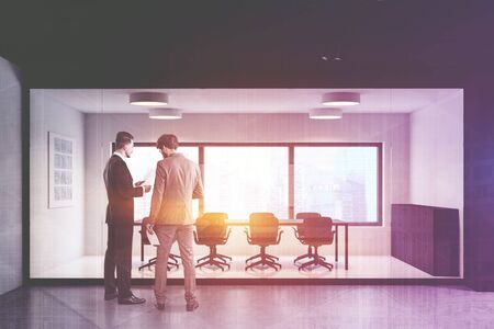 Two successful businessmen discussing work near panoramic office meeting room with white and glass walls, conference table and graphs on whiteboard. Corporate lifestyle. Toned image double exposureの写真素材