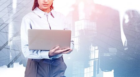 Portrait of unrecognizable young businesswoman using laptop in abstract blurry city. Concept of internet connection and education. Toned image double exposureの写真素材