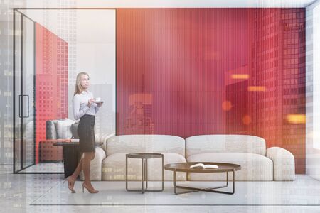 Smiling blonde woman in formal clothes standing in bright living room with red and white walls, comfortable sofa with round coffee tables and bedroom in background. Toned image double exposureの写真素材