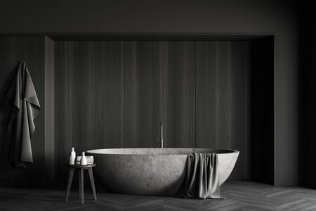 Interior of modern bathroom with grey and dark wooden walls, comfortable stone bathtub and chair with towels and beauty products. 3d renderingの写真素材