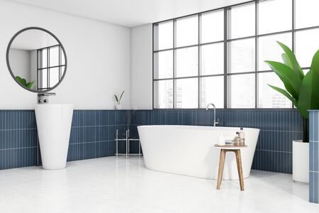 Corner of spacious panoramic bathroom with white and blue tiled walls, cozy bathtub, original sink with round mirror and window with blurry cityscape. 3d renderingの写真素材