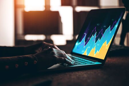 Hands of woman trader typing on laptop with digital financial graph in blurry office. Concept of...