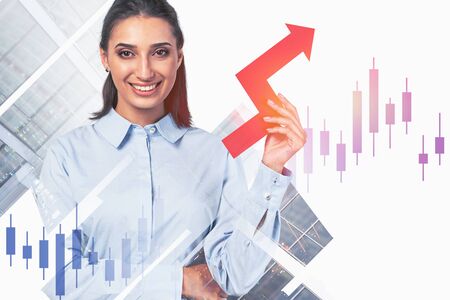 Cheerful young businesswoman with dark hair holding growing graph in abstract blurry city with double exposure of financial chart. Concept of growth, success and investment. Toned imageの写真素材