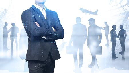Unrecognizable confident businessman standing with crossed arms in abstract city with his colleagues in background and double exposure of blurry cityscape. Concept of teamwork. Toned imageの写真素材