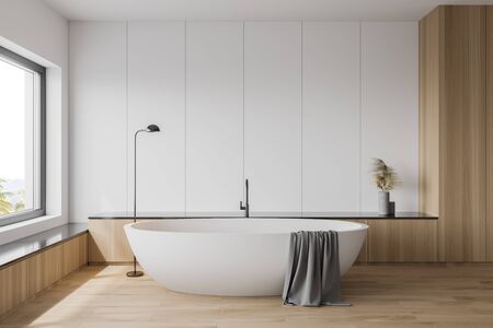 Interior of comfortable bathroom with white and wooden walls, wooden floor, comfortable white bathtub and window with blurry tropical view. 3d renderingの写真素材
