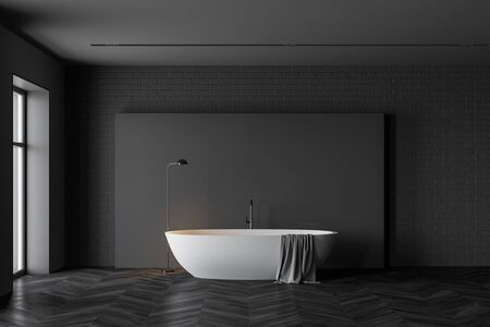 Interior of spacious minimalistic bathroom with grey and black brick walls, dark wooden floor, comfortable white bathtub and window. 3d renderingの写真素材