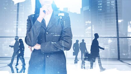 Unrecognizable thoughtful businesswoman and her colleagues walking in panoramic office with double exposure of blurry cityscape. Concept of leadership. Toned imageの写真素材