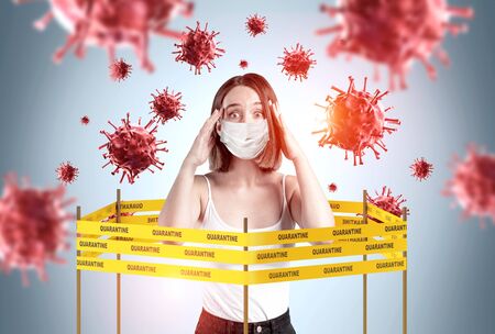 Portrait of panicking young European woman in mask inside of coronavirus quarantine tape barrier over grey background with blurry viruses around her. Concept of 2019 ncov pandemicの写真素材