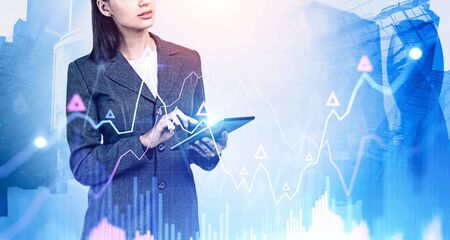 Unrecognizable woman trader using tablet in blurry city with double exposure of growing digital...