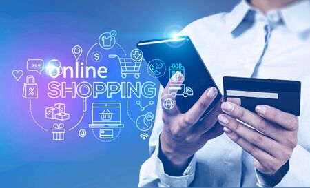 Hands of unrecognizable young businesswoman using smartphone and credit card over blurry blue background with double exposure of online shopping interface. Toned imageの写真素材