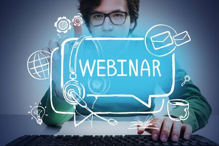 Handsome young man in glasses typing on keyboard over blurry gray background and using creative webinar interface. Toned imageの写真素材