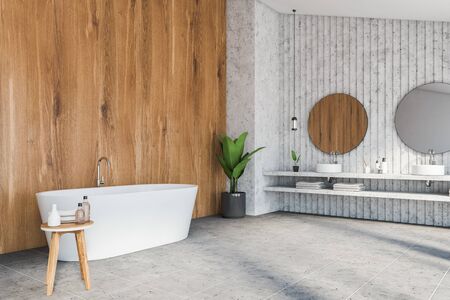 Corner of luxury attic bathroom with stone and wooden walls, tiled floor, double sink with two round mirrors and comfortable bathtub. 3d renderingの写真素材