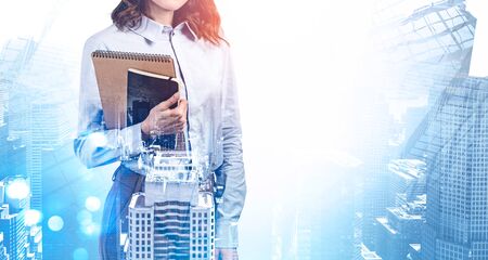 Unrecognizable young businesswoman with notebooks standing in blurry abstract city. Concept of education and leadership. Toned image double exposureの写真素材