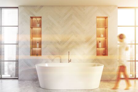 Blurry young woman walking in luxury bathroom with blue wooden walls, concrete floor, comfortable bathtub and shelves with beauty products. Toned imageの写真素材