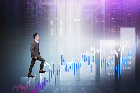 Young Asian businessman climbing bar chart in abstract panoramic city with double exposure of blurry financial graph and data center. Concept of stock market and fintech. Toned imageの写真素材